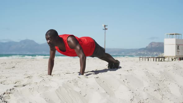 Focused african american man doing press ups on the beach, exercising outdoors by the sea alt