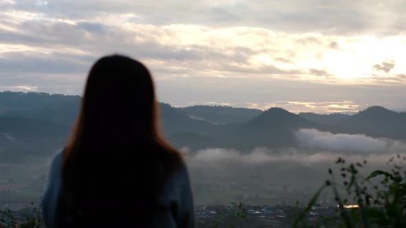 Blurred rear view of a female traveler looking at a beautiful mountain views on foggy day