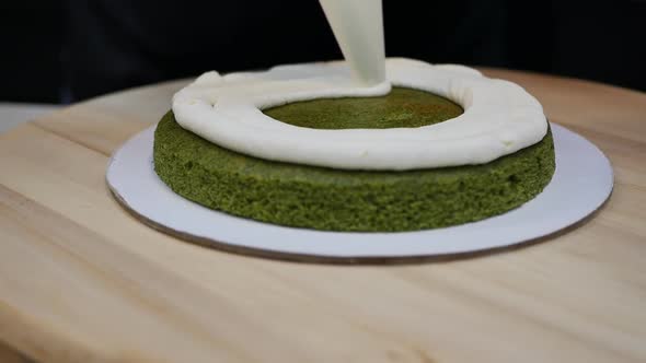 Pastry Chef Squeezes Butter Cream Out of a Bag Onto a Green Spinach Biscuit alt