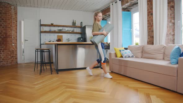 Fit Woman Folding Exercise Mat on Wooden Floor Before Working Out at Home alt