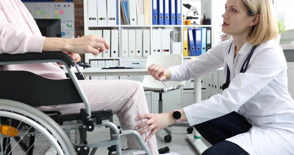Female Orthopedic Doctor Hit Woman Sitting in Wheelchair in Clinic Hammer Knee alt