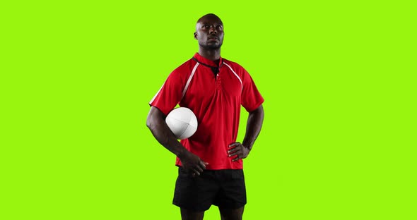 Professional Rugby Player Standing and Holding a Ball on Green Background alt