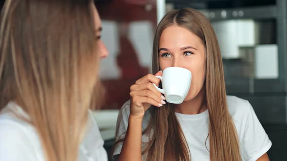 Two Women Friends in a Kitchen Drinking Coffee Talking and Having Fun alt