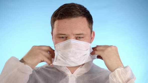 Caucasian Man in White Protective Jumpsuit Puts a Medical Mask on Face
