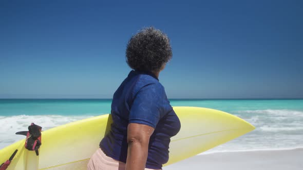 Senior woman walking with surfboard alt