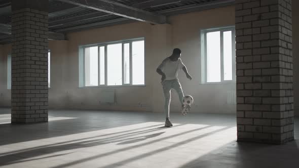 Black Man Football Soccer Player Practicing Tricks Kicks and Moves with Ball Inside Empty Covered alt