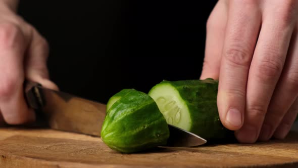 Slicing fresh cucumber on wooden the cutting Board. Black background. Close up.4k