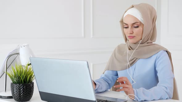 Young Muslim Woman Is Listening Music in Earphones Using Laptop and Enjoying It alt