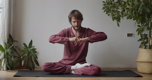 Bearded Master Massaging Fingers on Thailand Technique Sitting Indoors on Yoga Mat. Young Man
