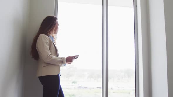 Biracial businesswoman standing using smartphone by window in modern interiors alt