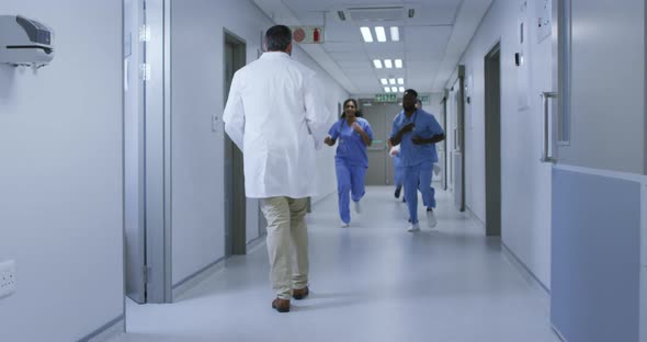 Diverse group of male and female doctors running urgently through hospital corridor alt