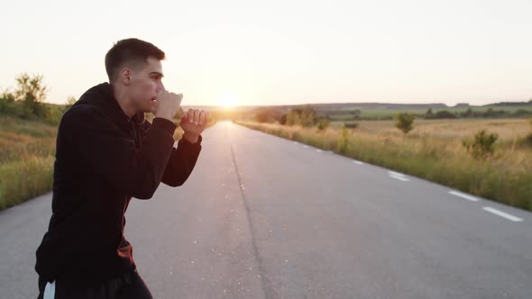 View of Young Kickboxer Training Kicks on Country Road Singly During Sunset alt