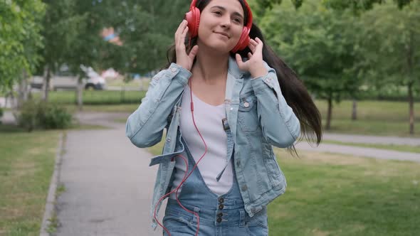 Beautiful Cheerful Girl Dancing Walking in the Park with Headphones alt