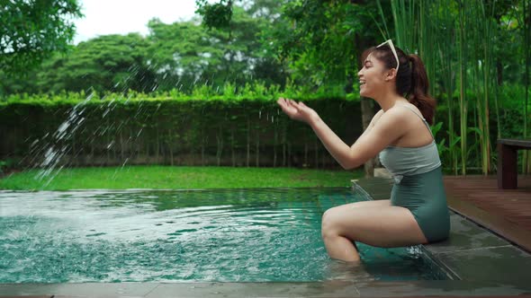 woman sitting on edge of swimming pool and playing water splashing