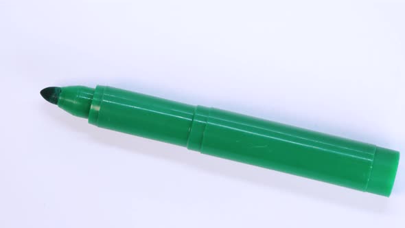 Green marker pen rotating on white surface background, macro shot close up view detail. alt