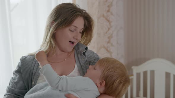 Motherhood, Beautiful Loving Woman Shakes in Arms of Her Dear Little Male Child, Sings Him Lullaby alt