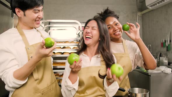 Three young cooking class students happy, fun teasing with fruits in a kitchen. alt