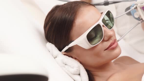 Close-up of Beautician Using Neodymium Laser on Woman Face in Protection Glasses alt