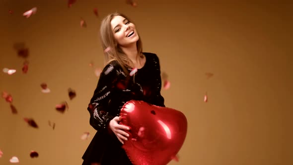 A Girl in a Black Dress with a Big Red Heart in Her Hands Rejoices Against the Background of Falling alt
