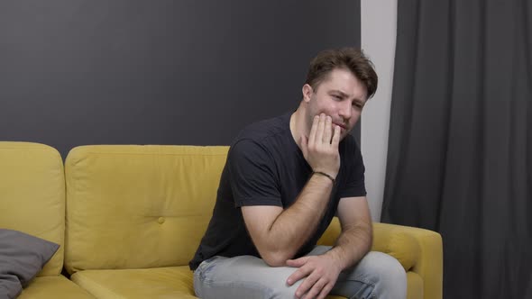 Unshaven Guy Sits on Sofa and Suffers From Toothache