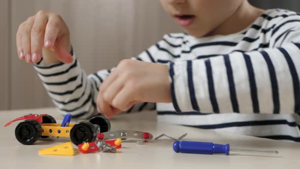 A Child Designs a Model of a Small Toy Car. A Happy Child Plays with a Constructor While Sitting at alt