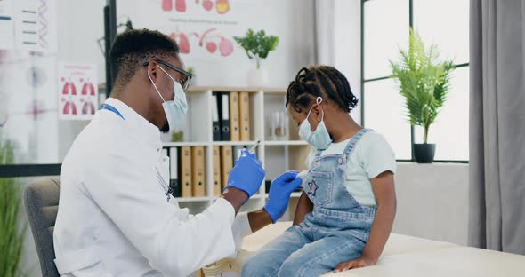Doctor in Facial Mask Doing Injection in Small girl's Arm During Her Visit to Clinic alt