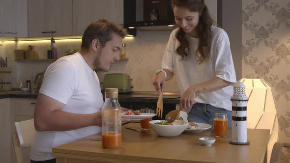 Couple Have Lunch at Home. Smiling Girl Puts Tuna Salad on Plate To Boyfriend