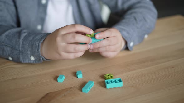 Caucasian Child Collects Toy Man From Plastic Constructor on Table Closeup alt