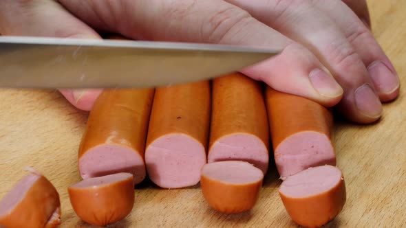 The cook cuts sausages. A man cuts several sausages at once with a knife into small round pieces