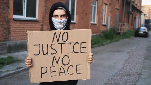 Man in Mask Stands with Cardboard Poster in Hands  NO JUSTICE NO PEACE