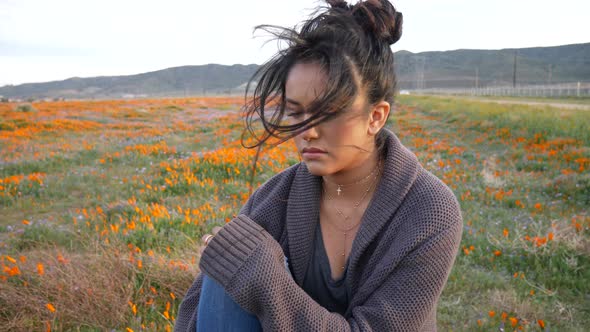 A young pretty girl sitting on a rock in a field of wild flowers looking sad and lonely with black h alt