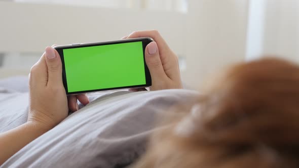 Woman at home relaxing in bed while holds green screen gadget 4K 2160p 30fps UltraHD footage - Green