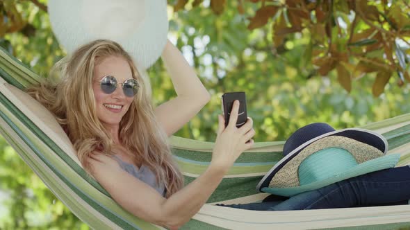 Smiling blonde woman with sunglasses using smartphone