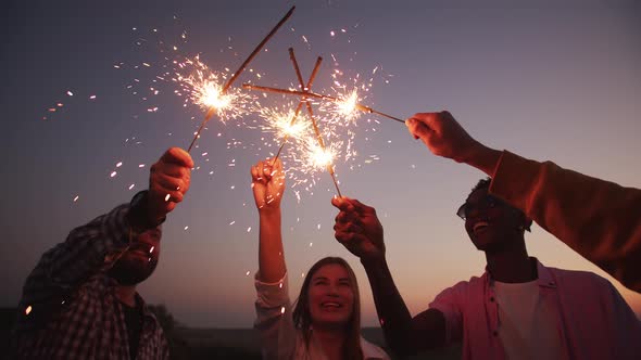 Close up hands holding sparklers group of friends celebrating waving sparkler fireworks. alt