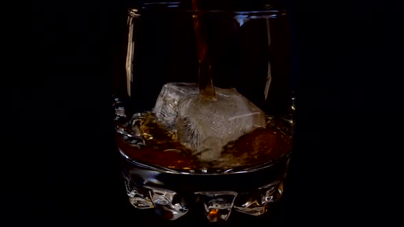 Pouring whiskey into a glass with ice on an isolated black background. Slow motion. alt