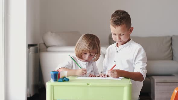 Portrait of Brother and Sister Sitting Together and Drawing at Home alt