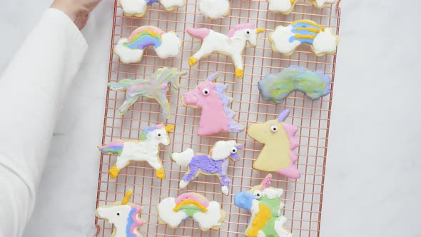 Unicorn shaped sugar cookies decorated with royal icing on pink plate. alt