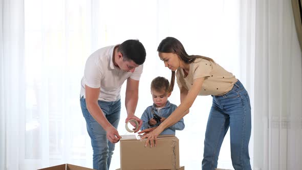 Young Couple Helps Small Son Pack Large Box with Duct Tape alt