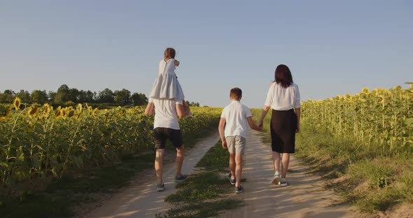 A Family With Two Children Walks In Nature On A Sunflower Field