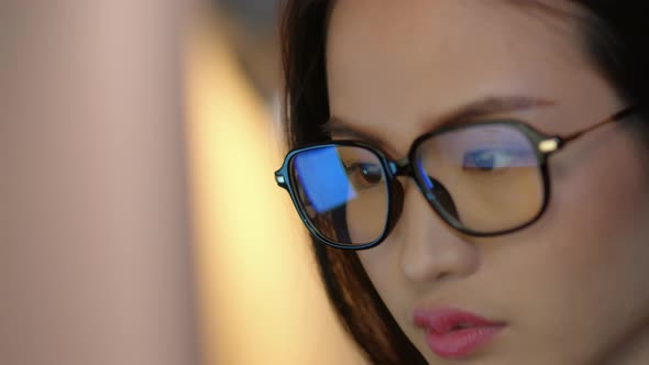 Close up asian businesswoman wearing glasses looking at computer screen working at night