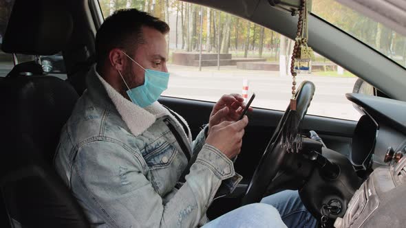 A Modern Young Man in a Medical Mask Driving Working on the Phone alt