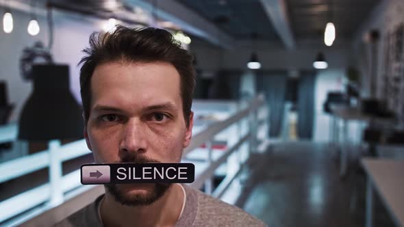 Man Looks Into the Camera and Holds a Sign in His Mouth That Says SILENCE