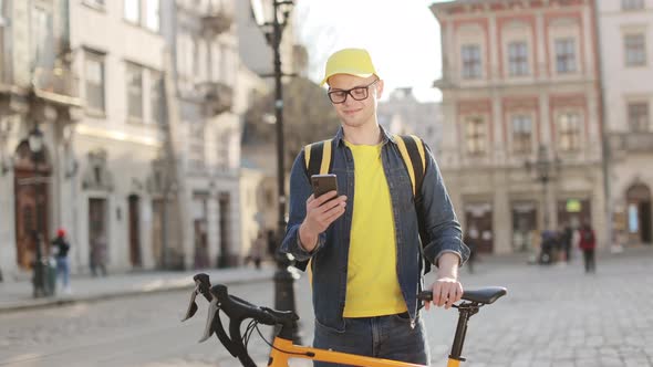 Portrait of a Happy Delivery Man Who is Standing and Texting on a Smartphone alt