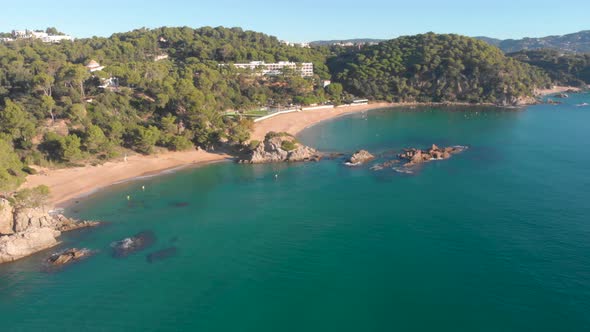 Aerial, drone shot, over rocky coast and turquoise sea, towards Lloret de Mar beach, Santa Cristina, alt