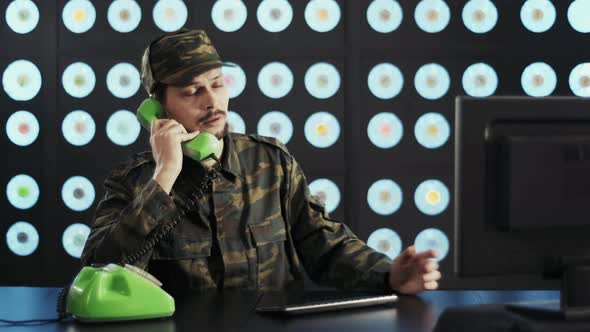 Man in Military Uniform Types on Keyboard Speaking on Old Green Telephone