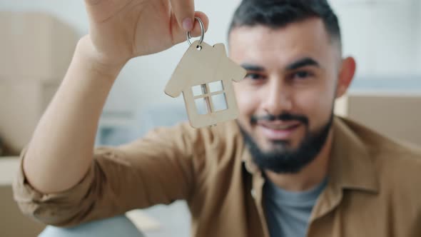Closeup of Male Hand Holding House Key Looking at Camera and Smiling Indoors in Light Room alt