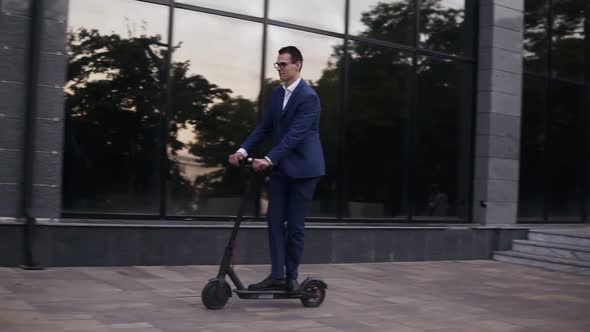 Young Businessman in Elegant Blue Suit and Glasses Riding an Electric Scooter for a Business Meeting alt