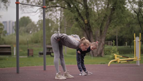  Mother and Daughter Doing Exercises on Open Air Sport Playground alt