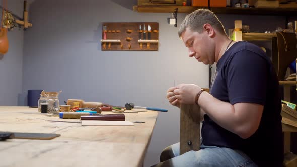 Tanner Sews a Needle Leather Product in the Studio. He Makes a Purse for Individual Design alt
