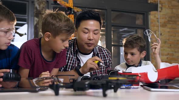 Asian Electronic Engineer with Caucasian Schoolchildren Working in Modern School alt